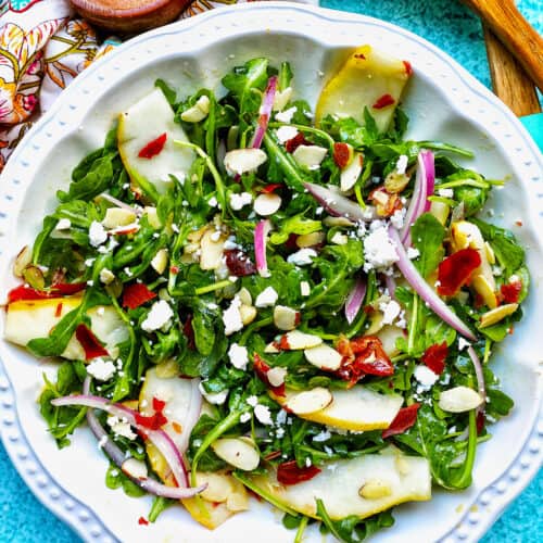 arugula, pears, prosciutto, and red onion salad in a white bowl.