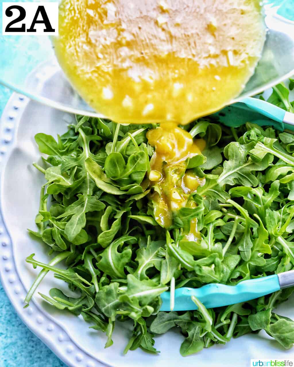 pouring salad dressing over a bowl of baby arugula.