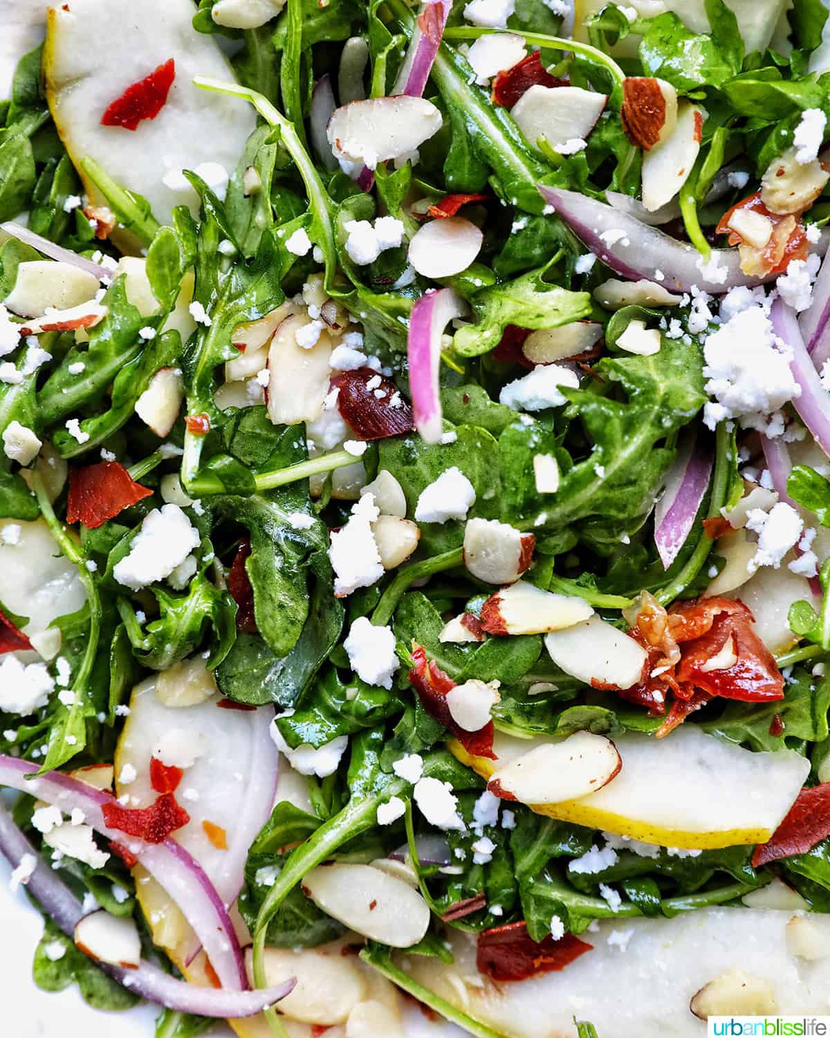 closeup of arugula pear salad with sliced almonds and sliced red onions.