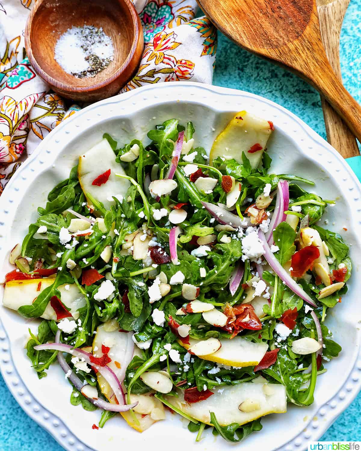 large bowl of arugula and pear salad with side of salt and pepper and a wooden spoon.