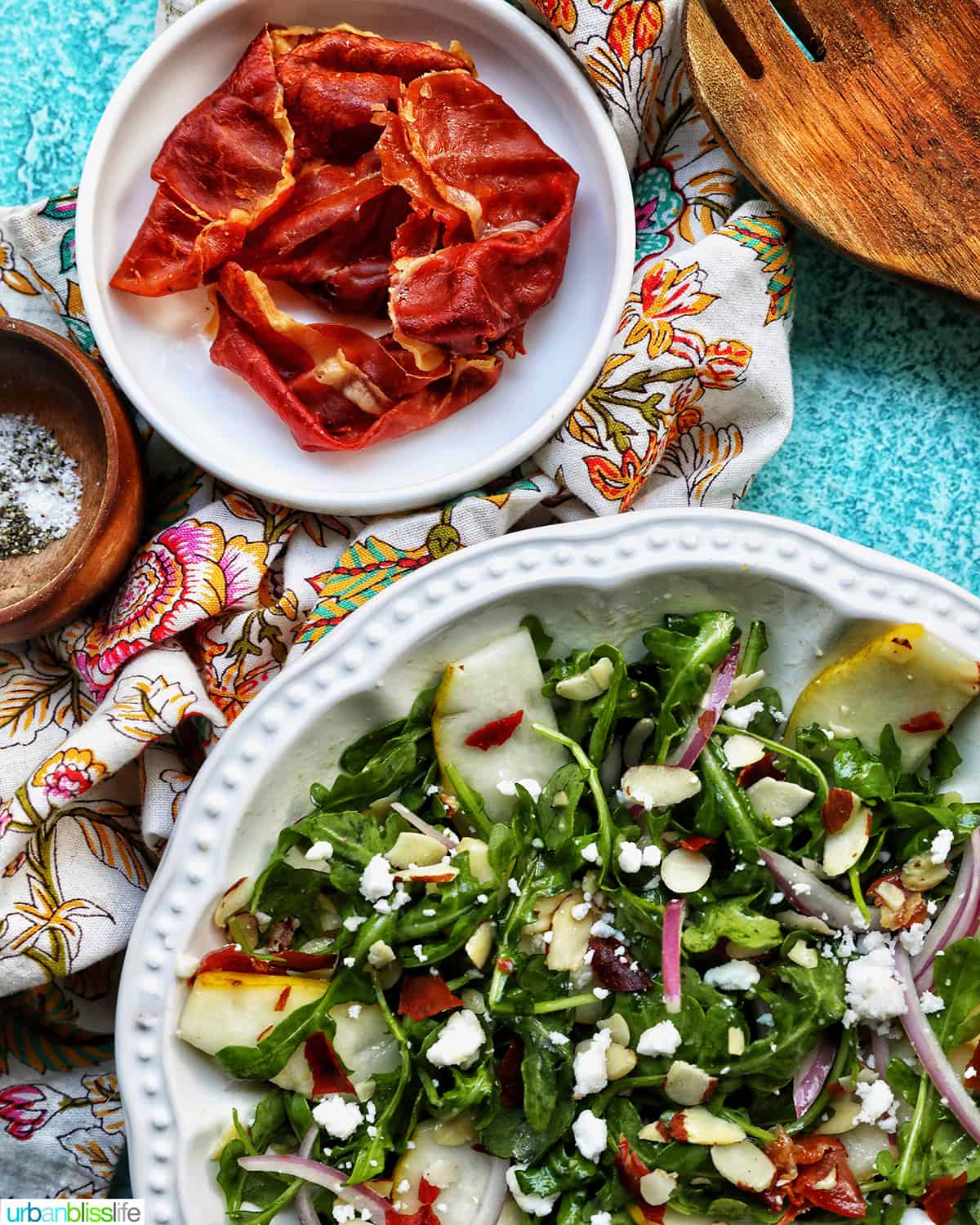 bowl of pear arugula salad with a bowl of crispy proscutto above it.