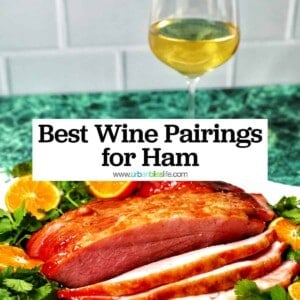 glass of white wine behind honey glazed ham sliced with oranges and herbs, and title text overlay.