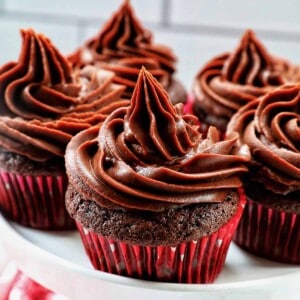chocolate cupcakes with chocolate fudge frosting stacked on a cake pedestal.