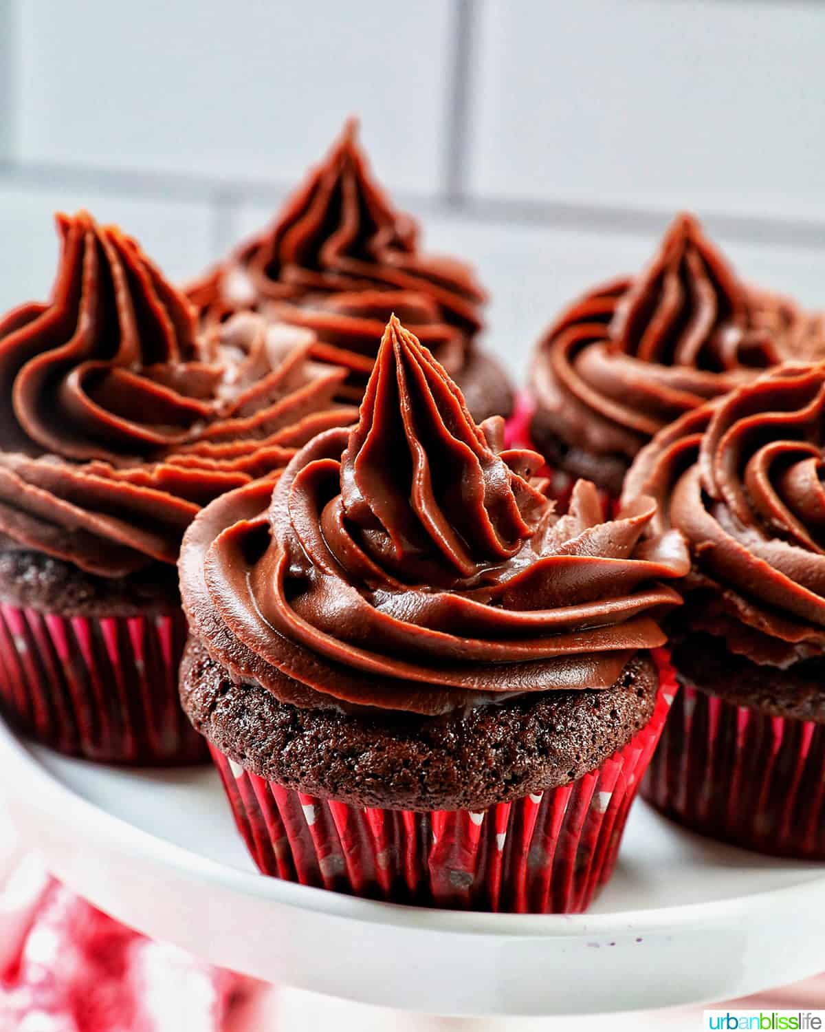 chocolate cupcakes with chocolate fudge frosting stacked on a cake pedestal.