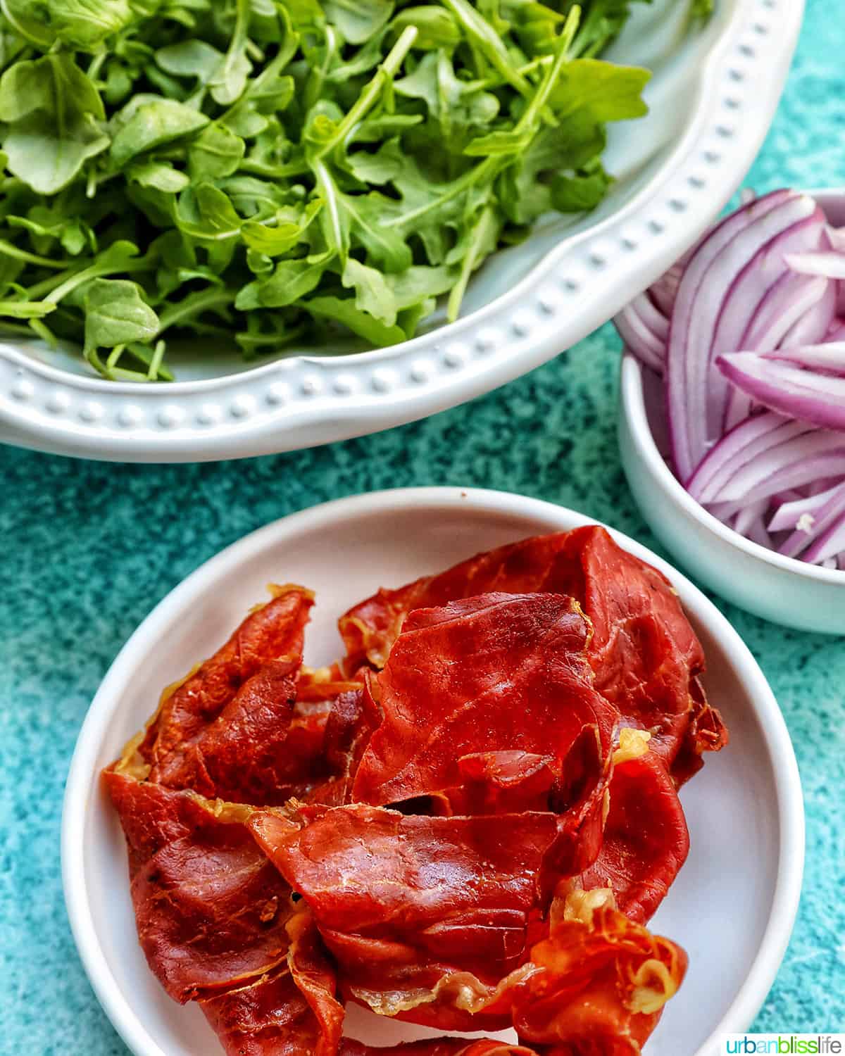 bowls of prosciutto, arugula, and red onions.