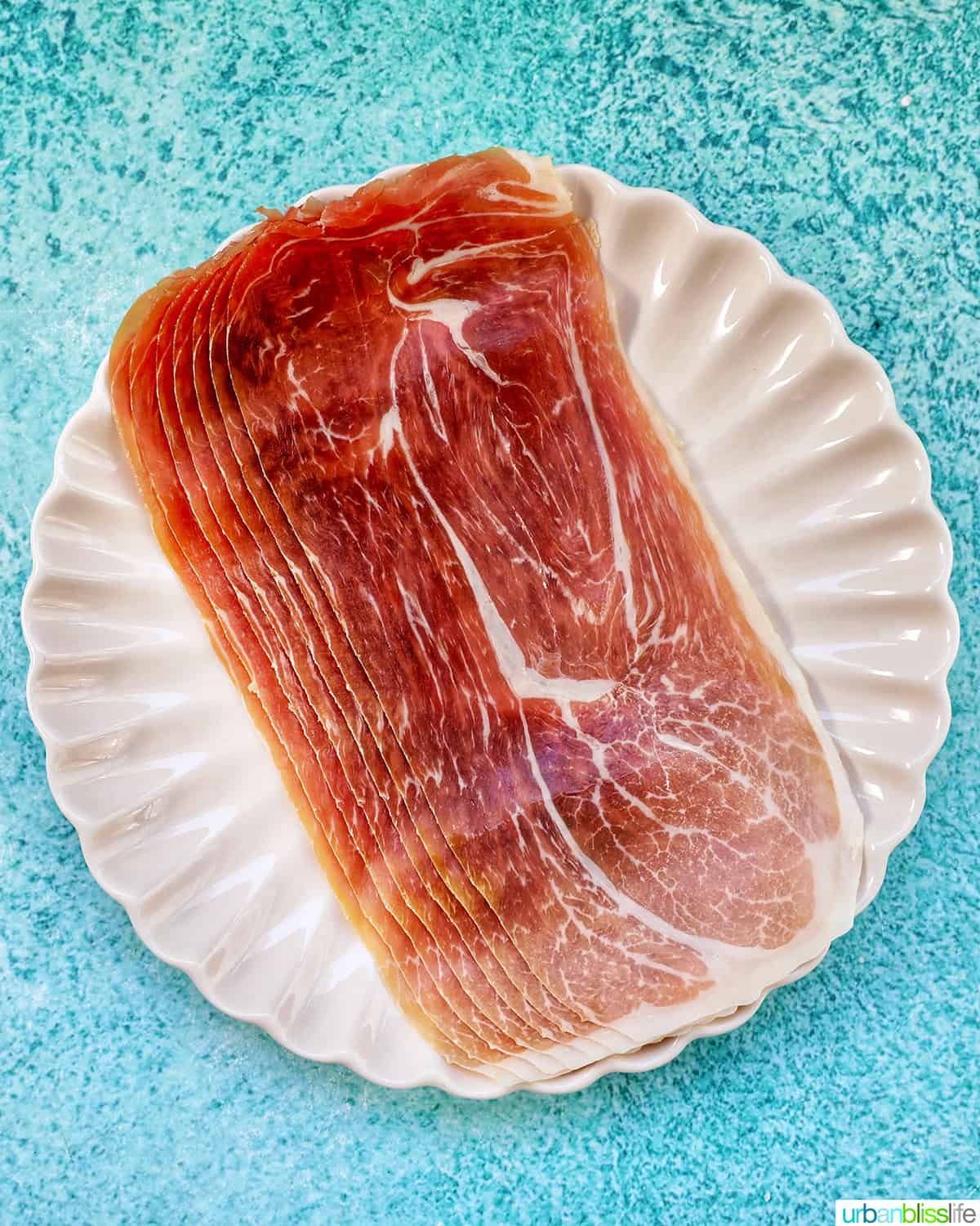prosciutto strips on a plate on a blue table.