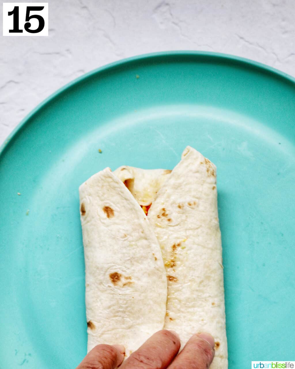 hand wrapping tortilla over on a plate.