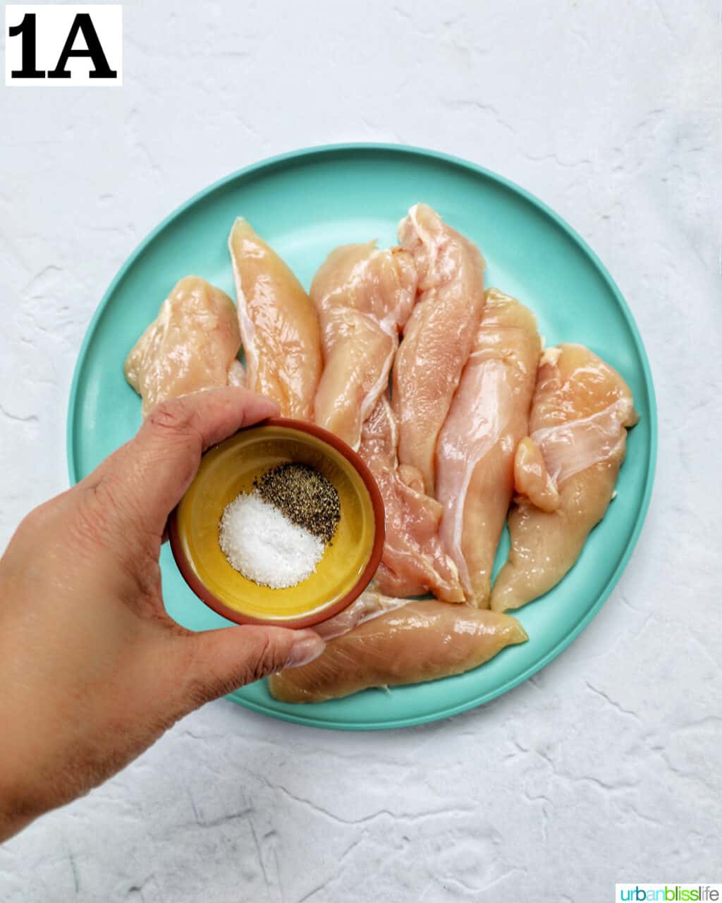 hand holding a small bowl of salt and pepper over a plate of chicken tenders.