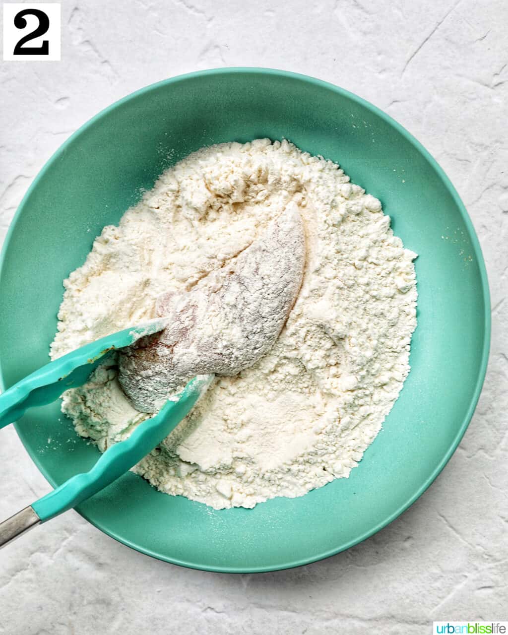 tongs dredging a chicken tender into flour.