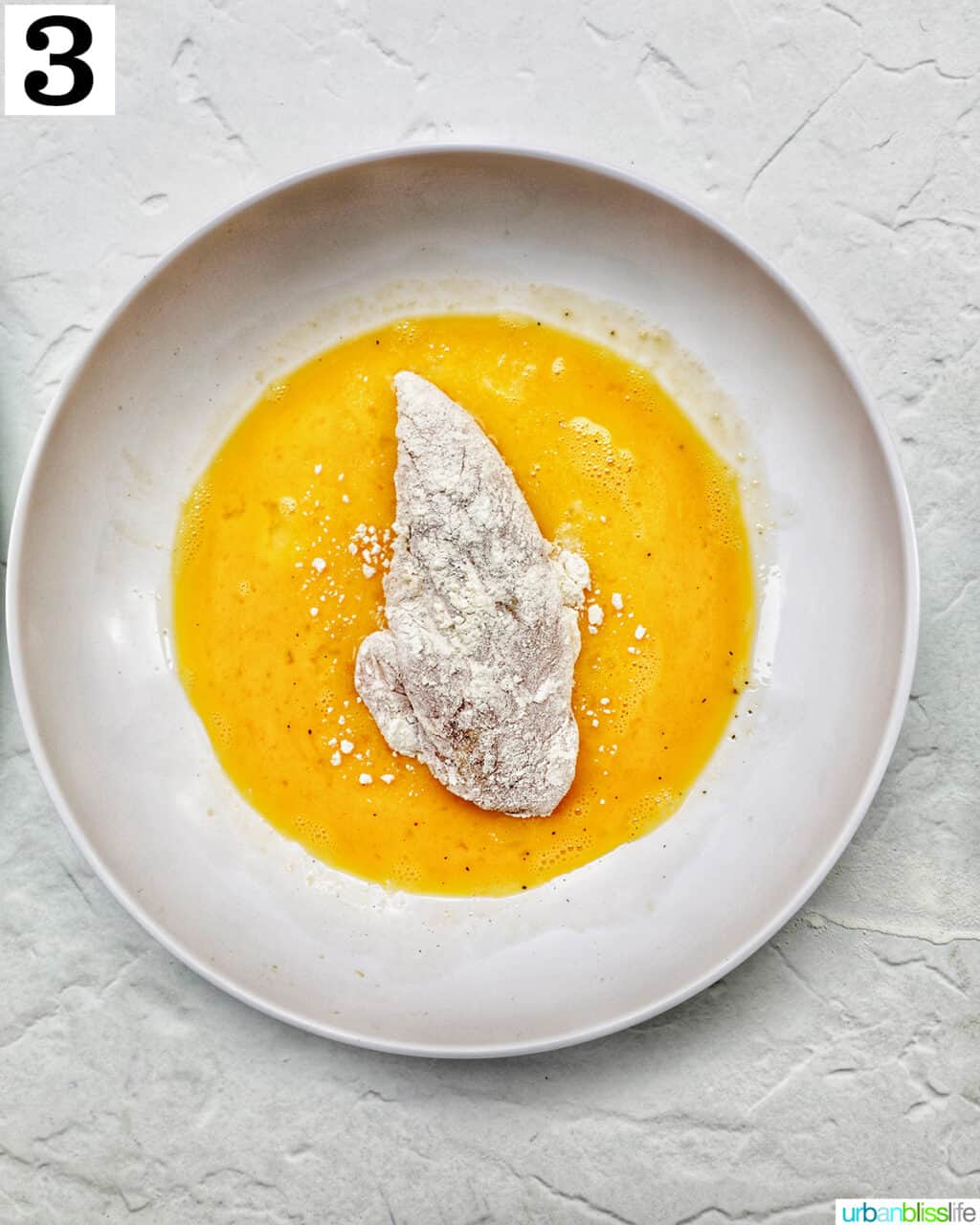 floured chicken tender in a bowl of beaten eggs.