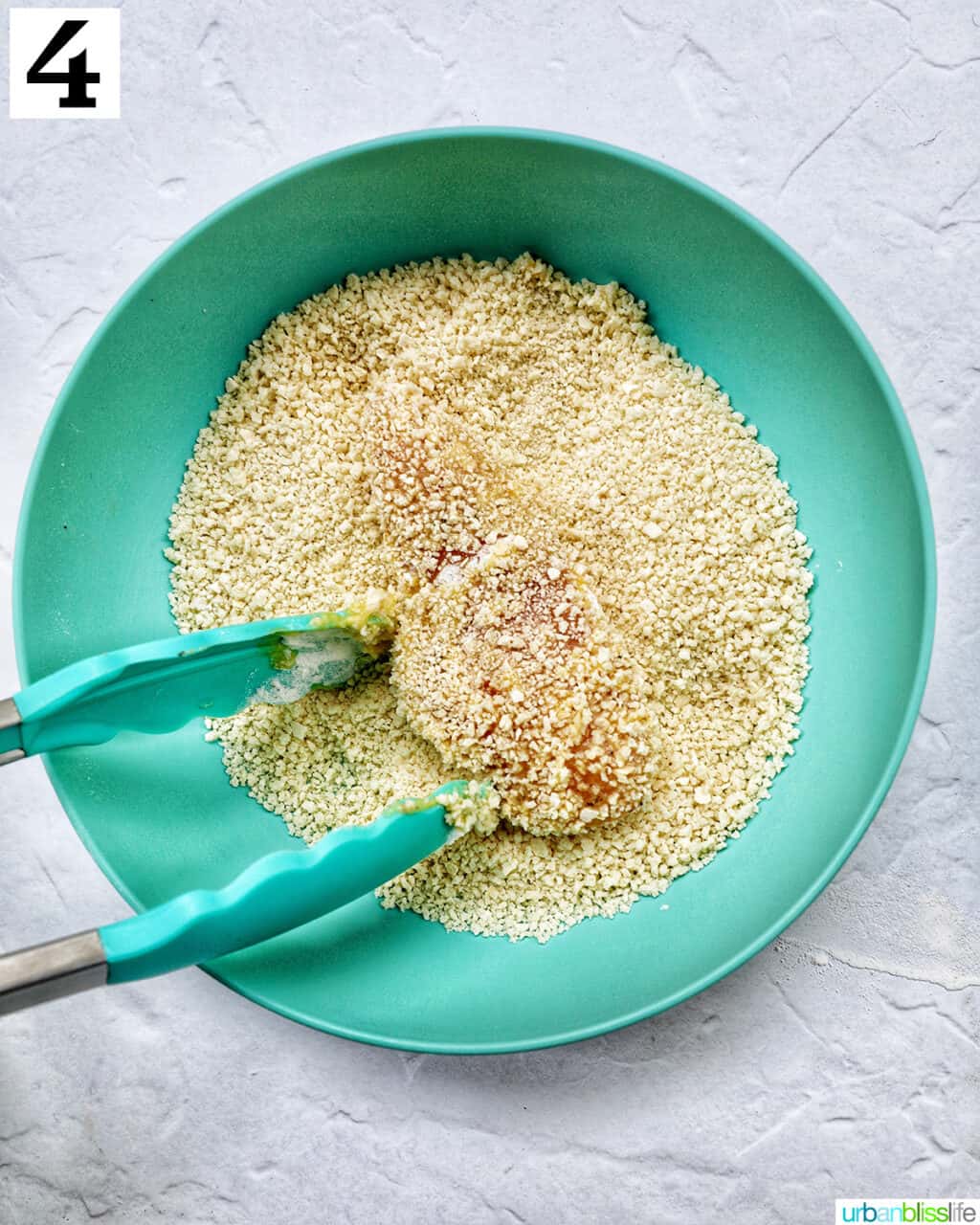 tongs tossing a chicken tender in a bowl of panko breadcrumbs.