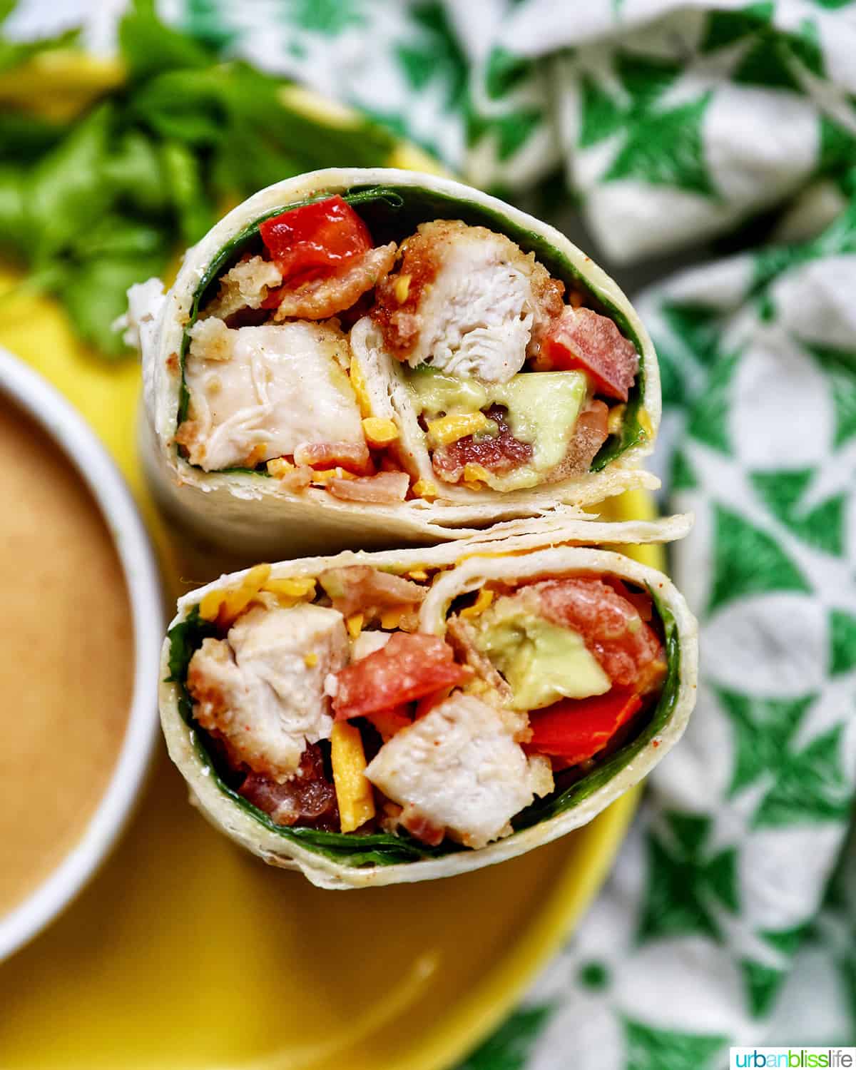 honey mustard chicken wraps sliced in half with the middle exposed next to honey mustard sauce and a green and white patterned napkin.