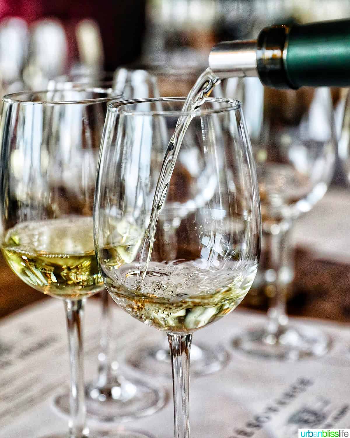 several glasses of white wine, with a bottle pouring white wine into one glass.