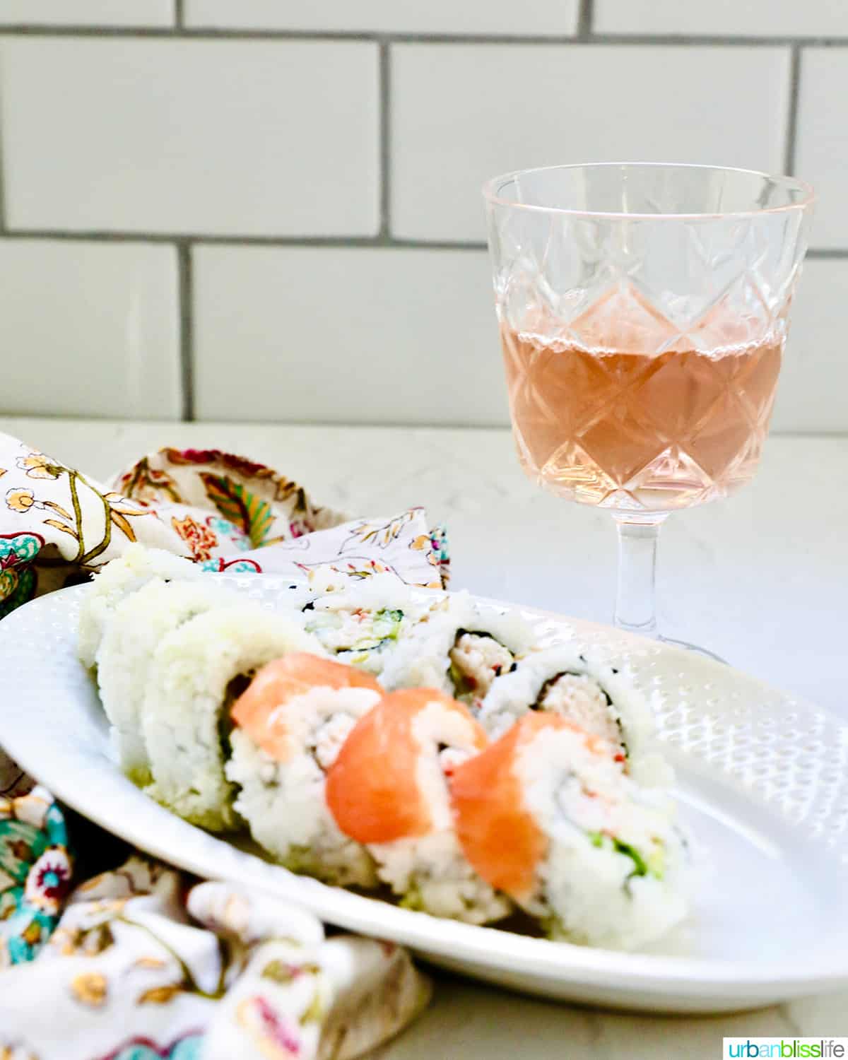 glass of rosรฉ wine with a plate of sushi rolls.