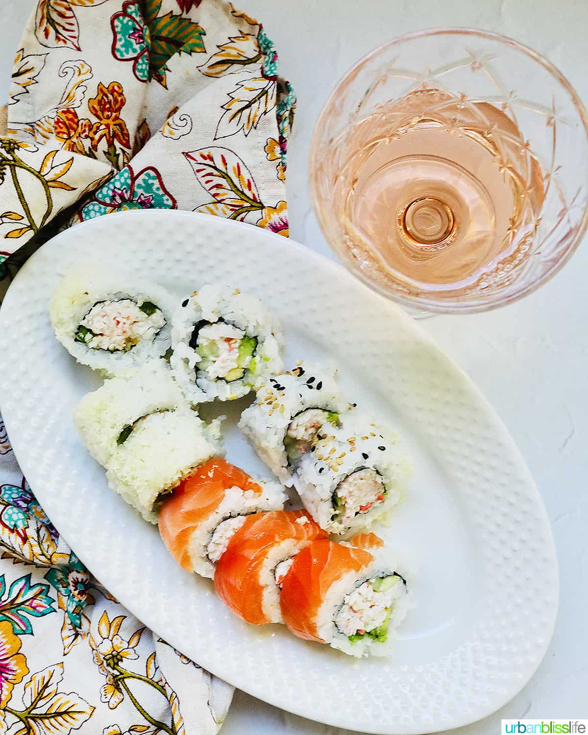 glass of rosé wine with a plate of sushi rolls.