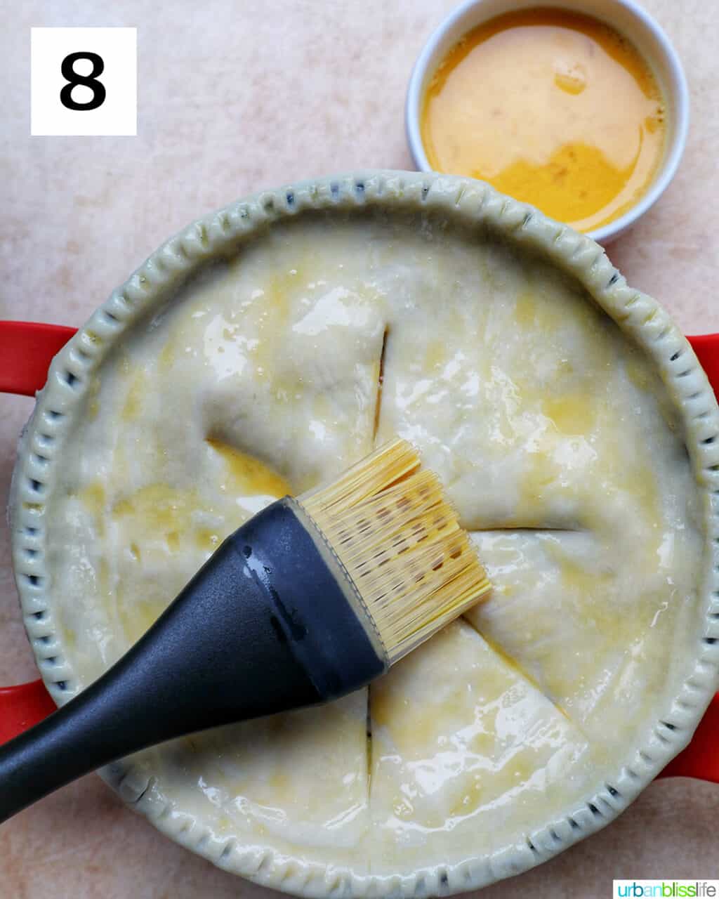pastry brush brushing egg wash over an unbaked pie crust.