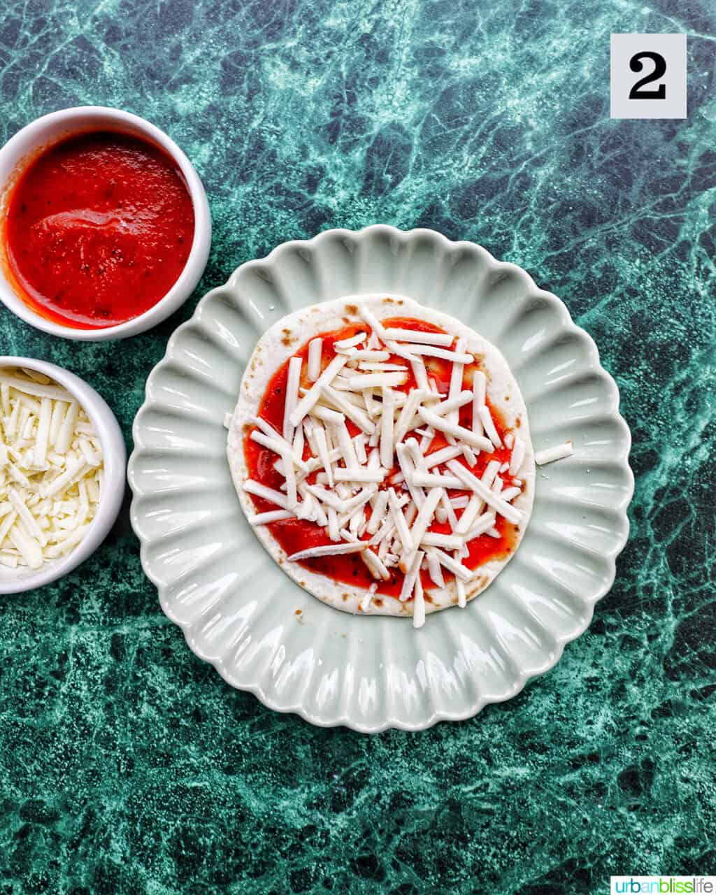 plate of a tortilla round with pizza sauce and shredded mozzarella.