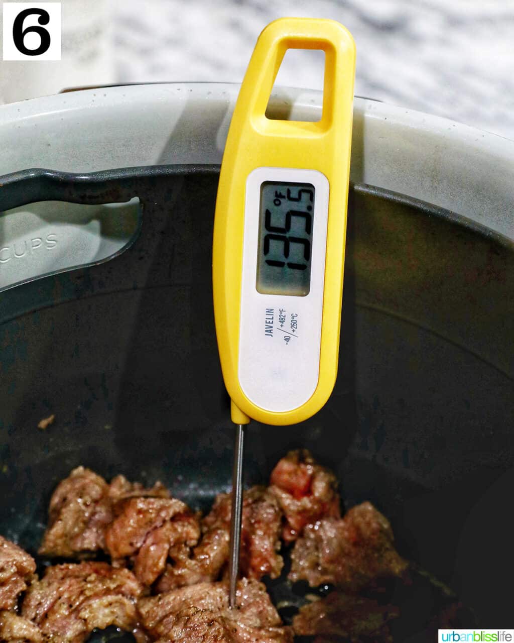 meat thermometer checking the internal temperature of steak tips in an air fryer basket.