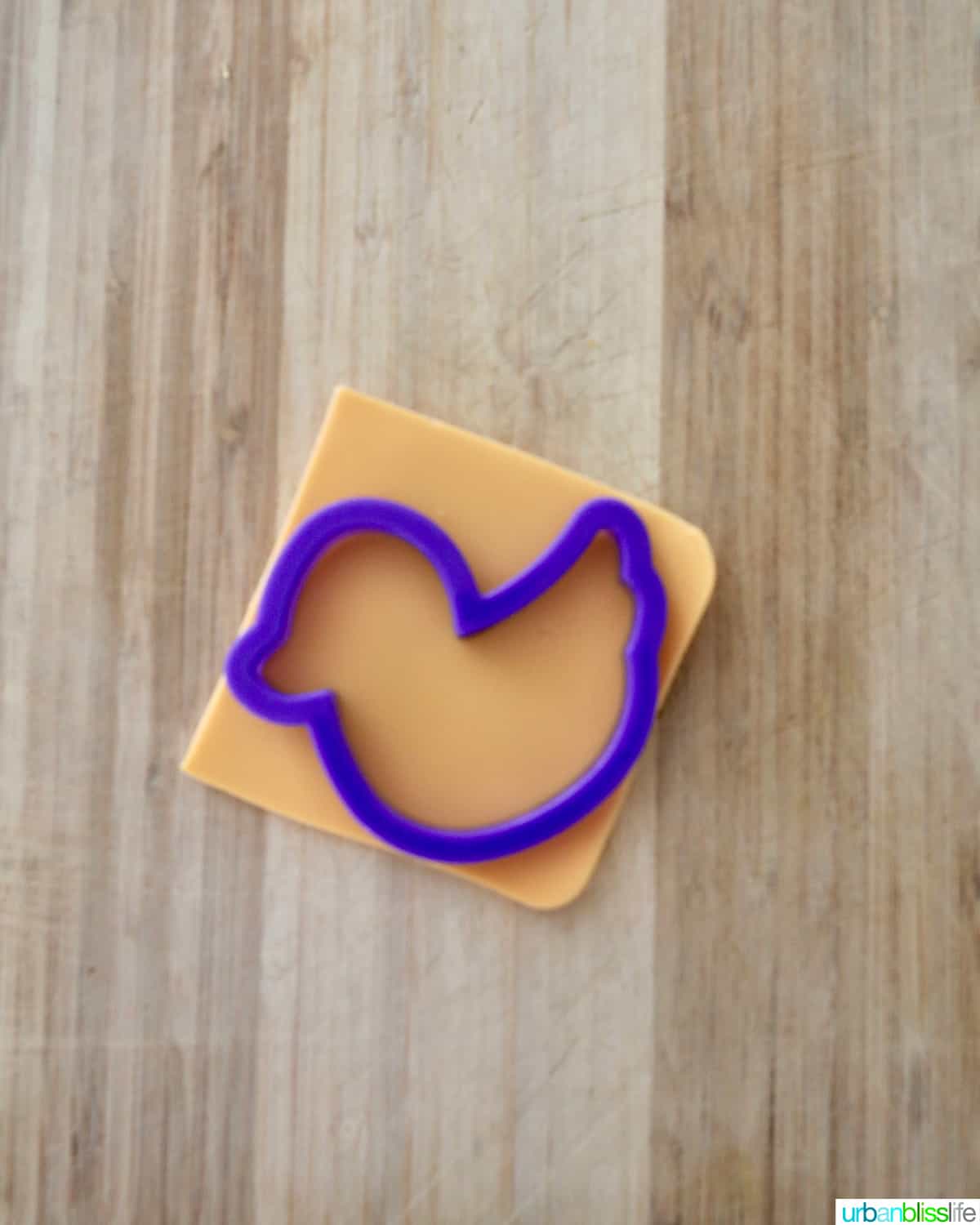 duck cookie cutter over a slice of cheese on a wooden cutting board.