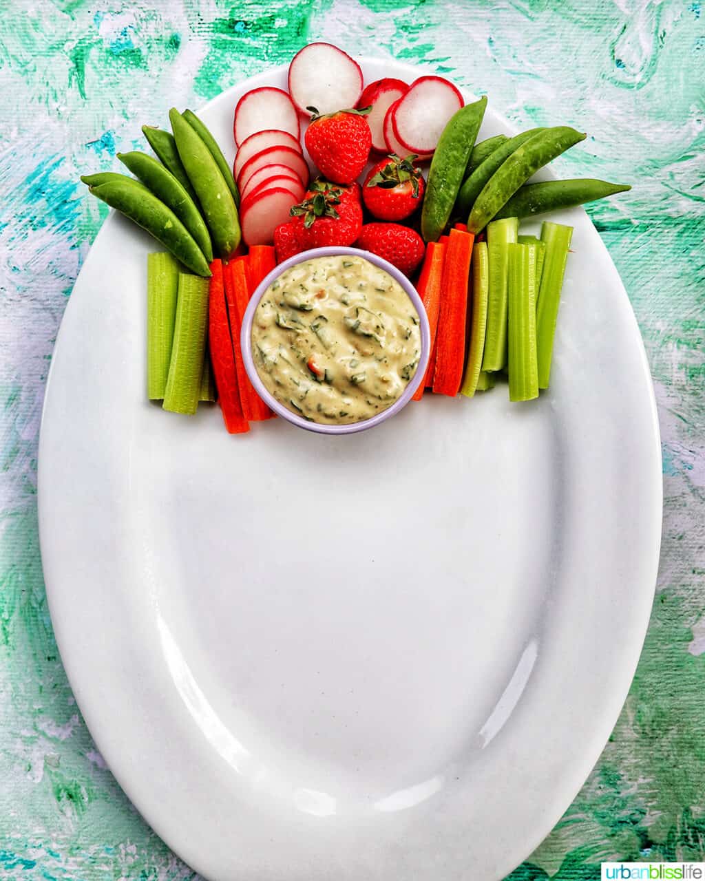 sliced vegetables with bowl of vegetable dip on a large white platter.