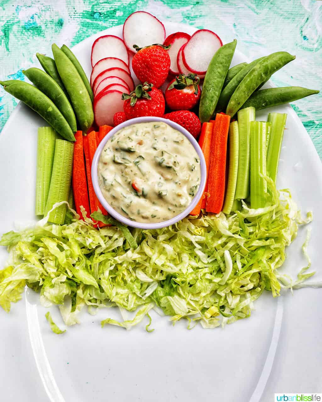 sliced veggies, shredded lettuce, and a bowl of vegetable dip on a large white platter.
