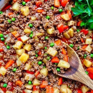 Filipino Beef Giniling (picadillo) in a large pan with a wooden spoon and side of parsley.