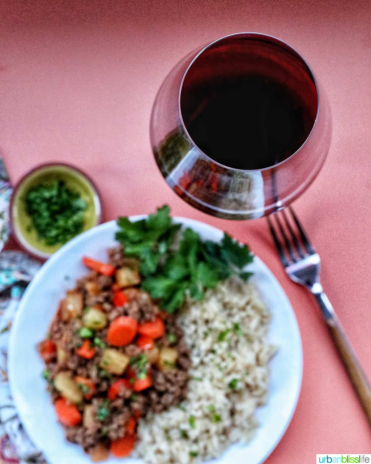 glass of red wine by a bowl of Filipino beef giniling over white rice.