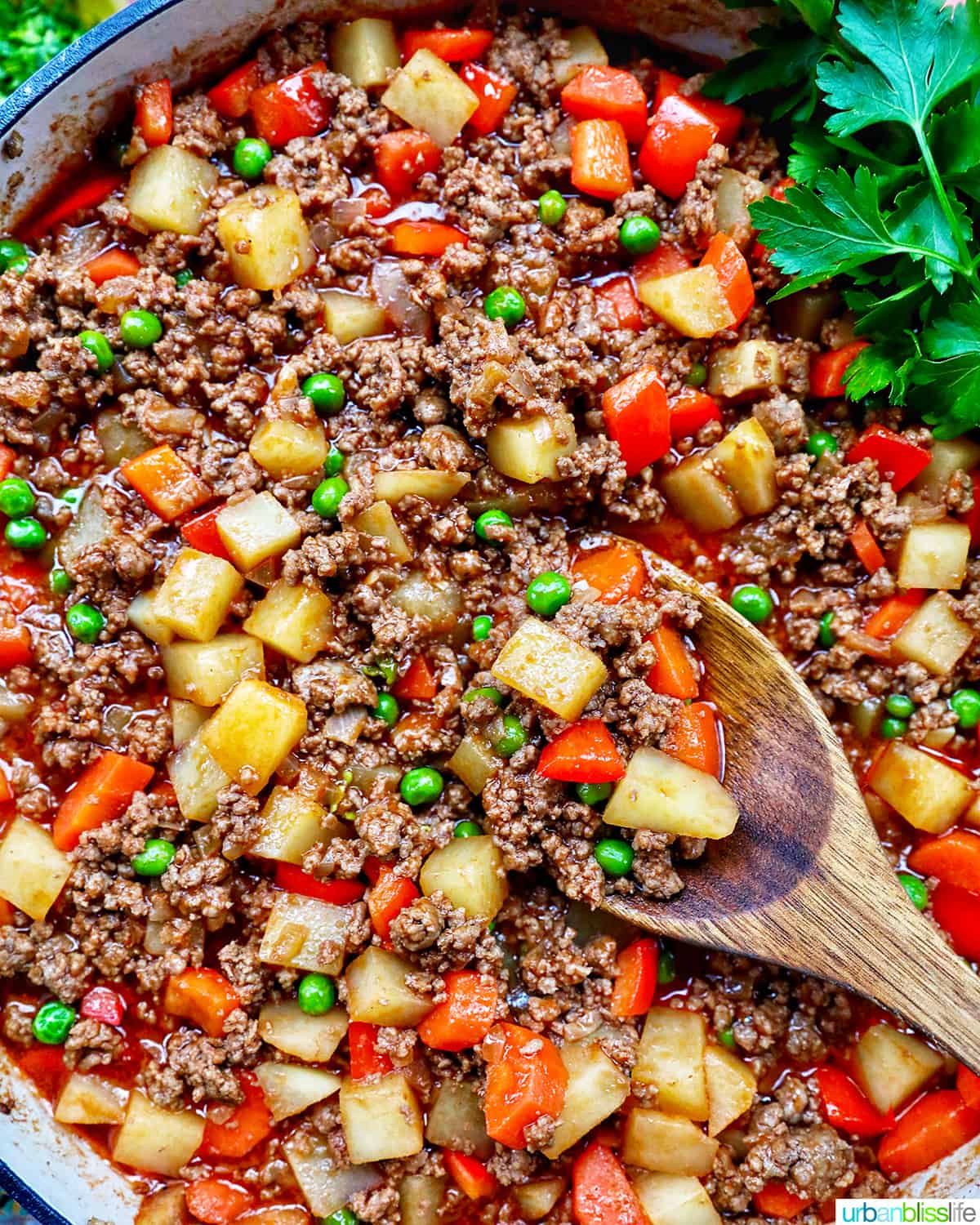 Filipino Beef Giniling (picadillo) in a large pan with a wooden spoon and side of parsley.