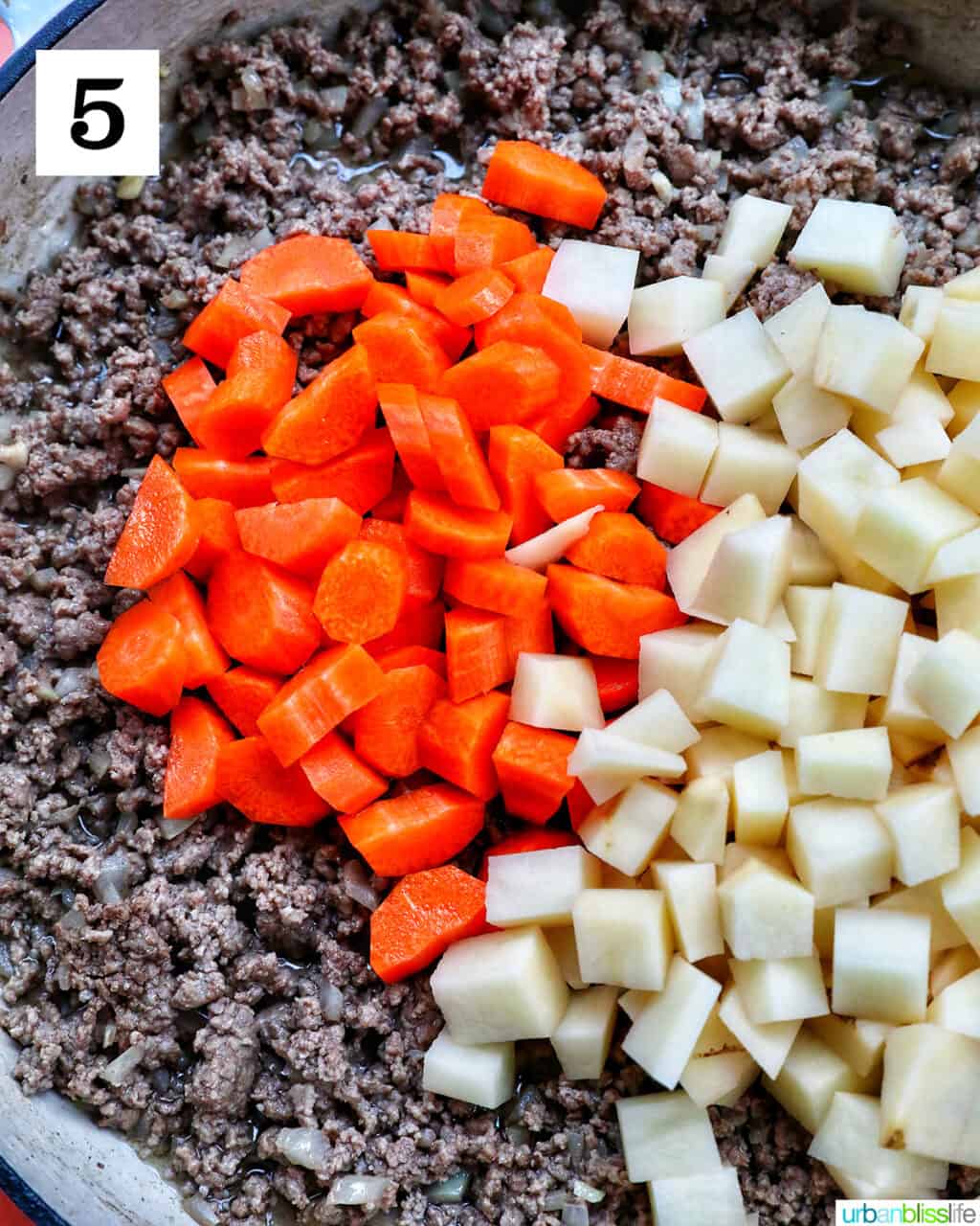 chopped carrots and potatoes over cooked ground beef in a large white pan.