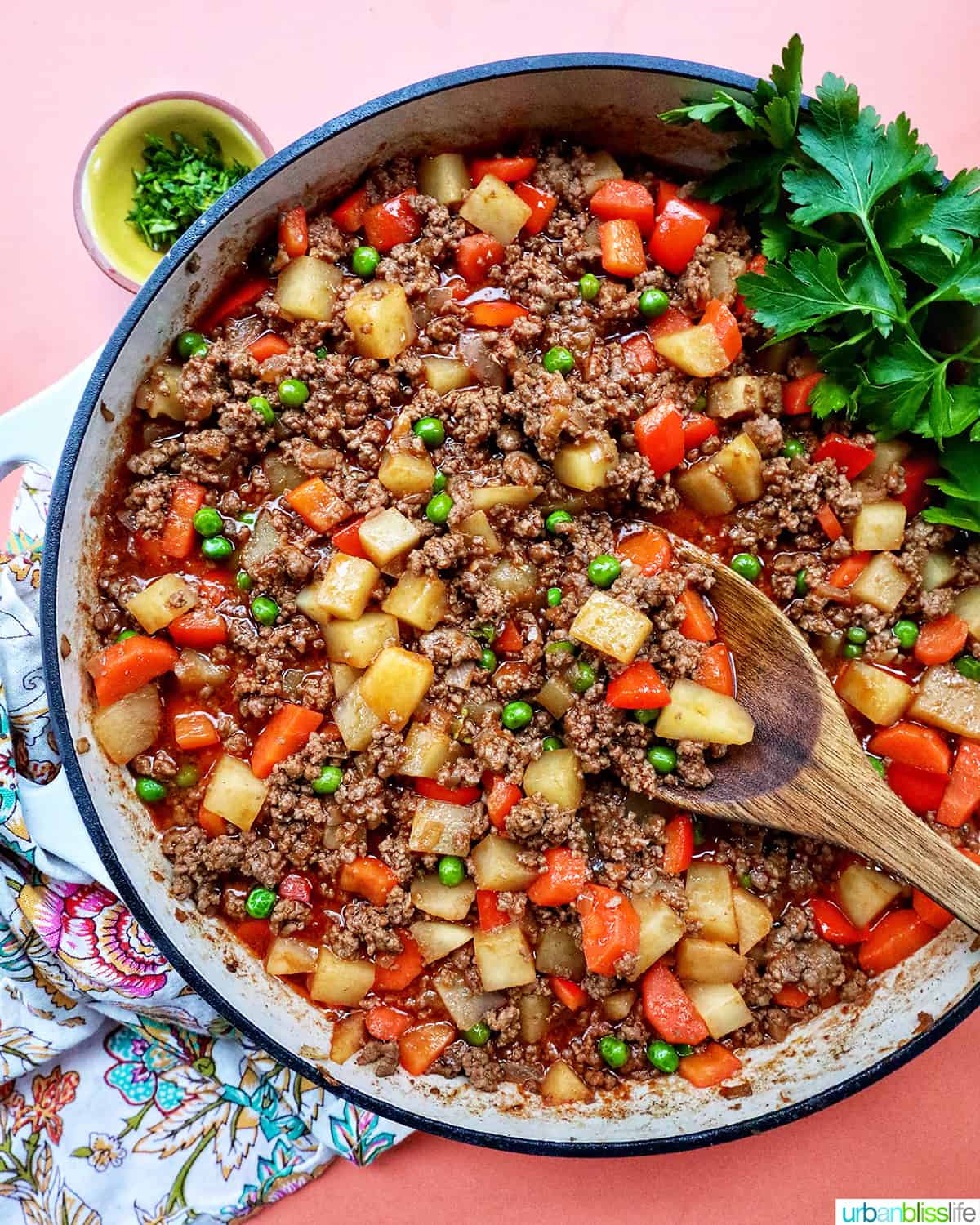Filipino Beef Giniling (picadillo) in a large pan with a wooden spoon and side of parsley.