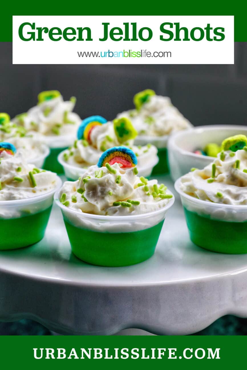 several green jello shots topped with whipped cream and colorful marshmallows on a cake pedestal.