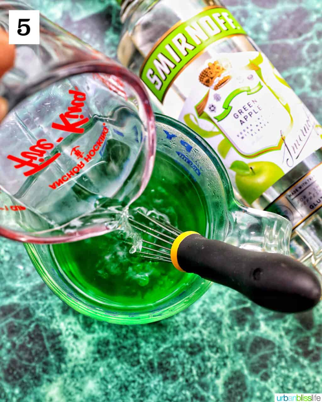 measuring cup pouring liquid into another bowl of green jello shot liquid.