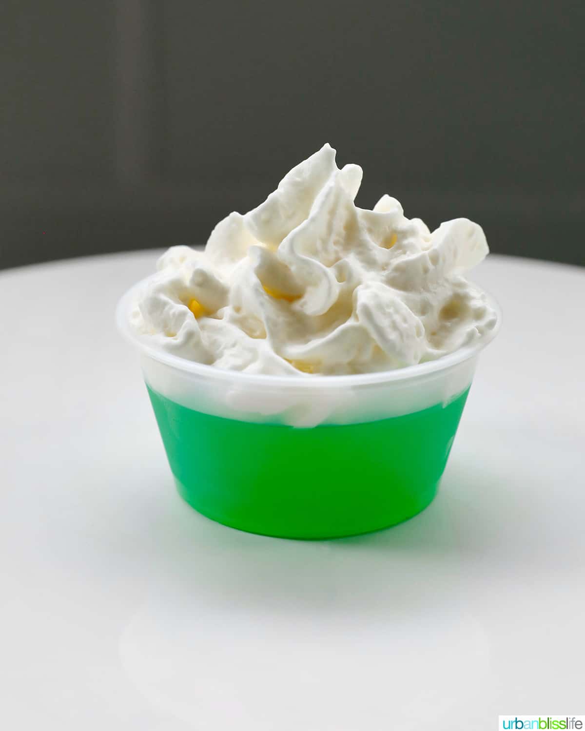 individual green jello shot topped with whipped cream on a white plate.