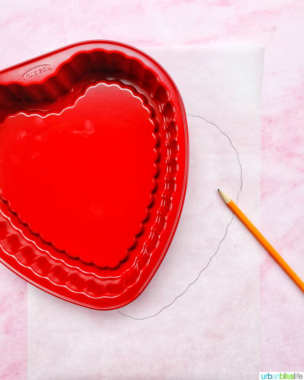 red heart-shaped baking pan over parchment paper and a pencil.