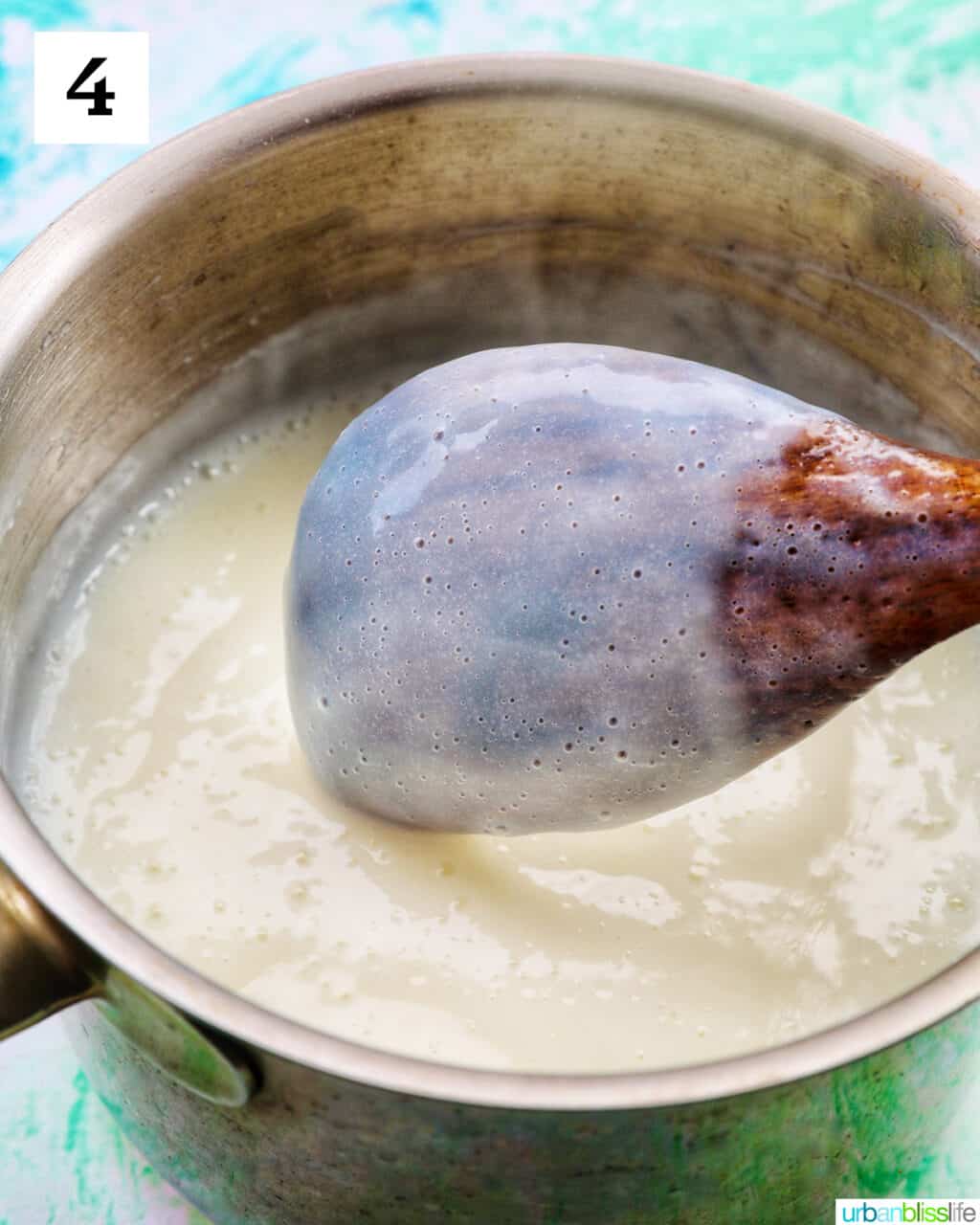 white vanilla pudding coating the back of a wooden spoon above a saucepan of vanilla pudding.