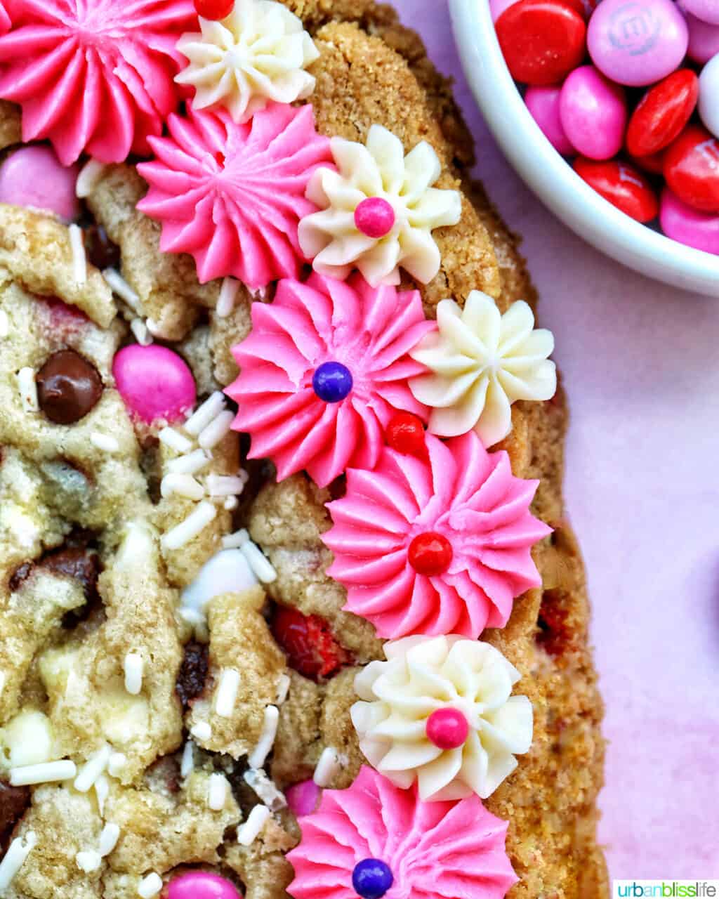 A heart-shaped Valentine's Day cookie cake with pink and white vanilla frosting and red, white, and pink M & M decorations.