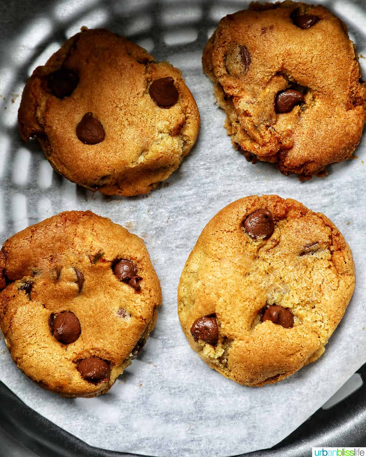 four chocolate chip cookies baked in an air fryer basket.