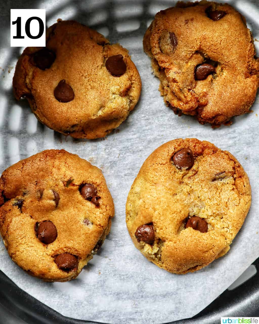 four chocolate chip cookies baked in an air fryer basket.