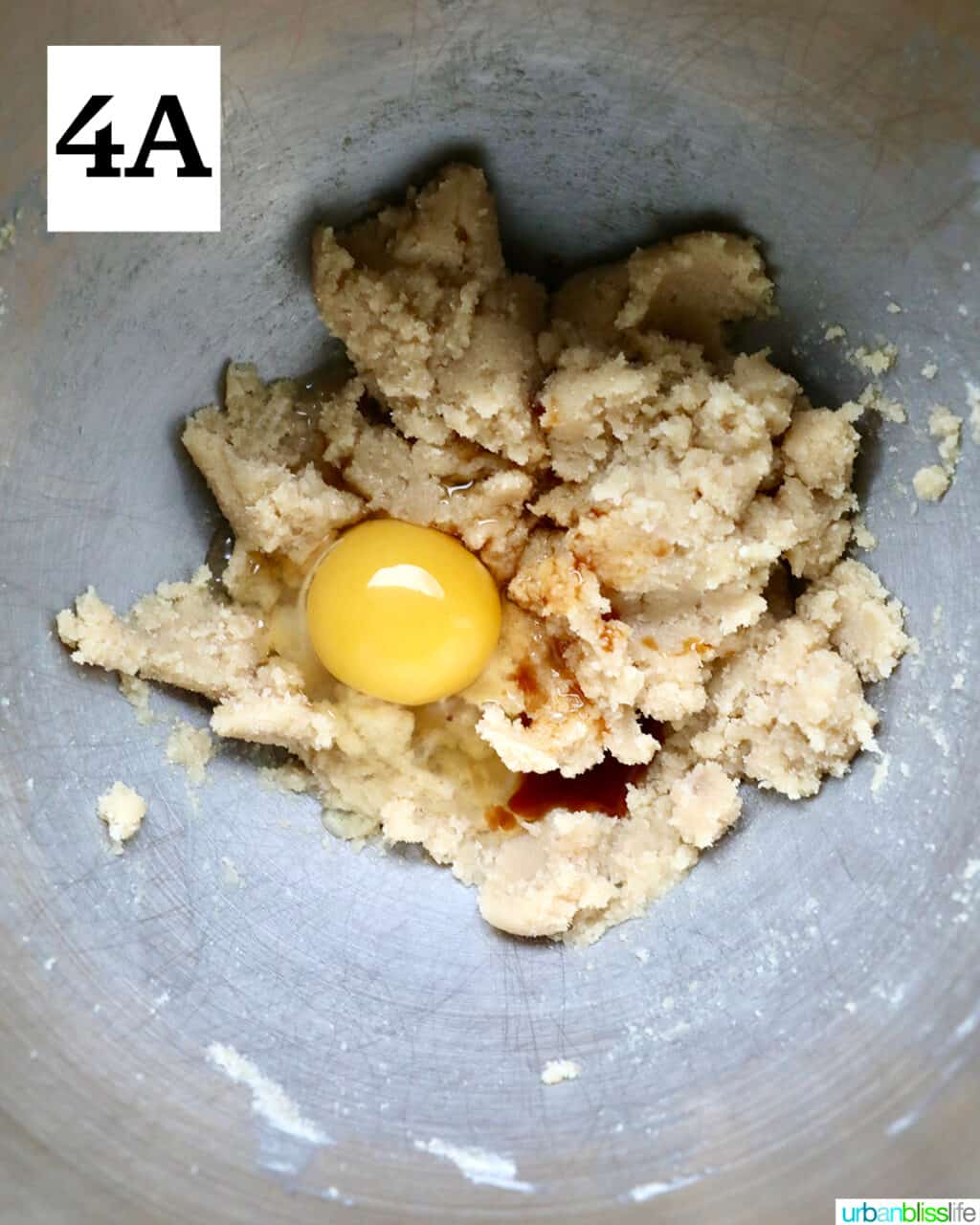 egg added to cookie dough batter in a stainless steel bowl.