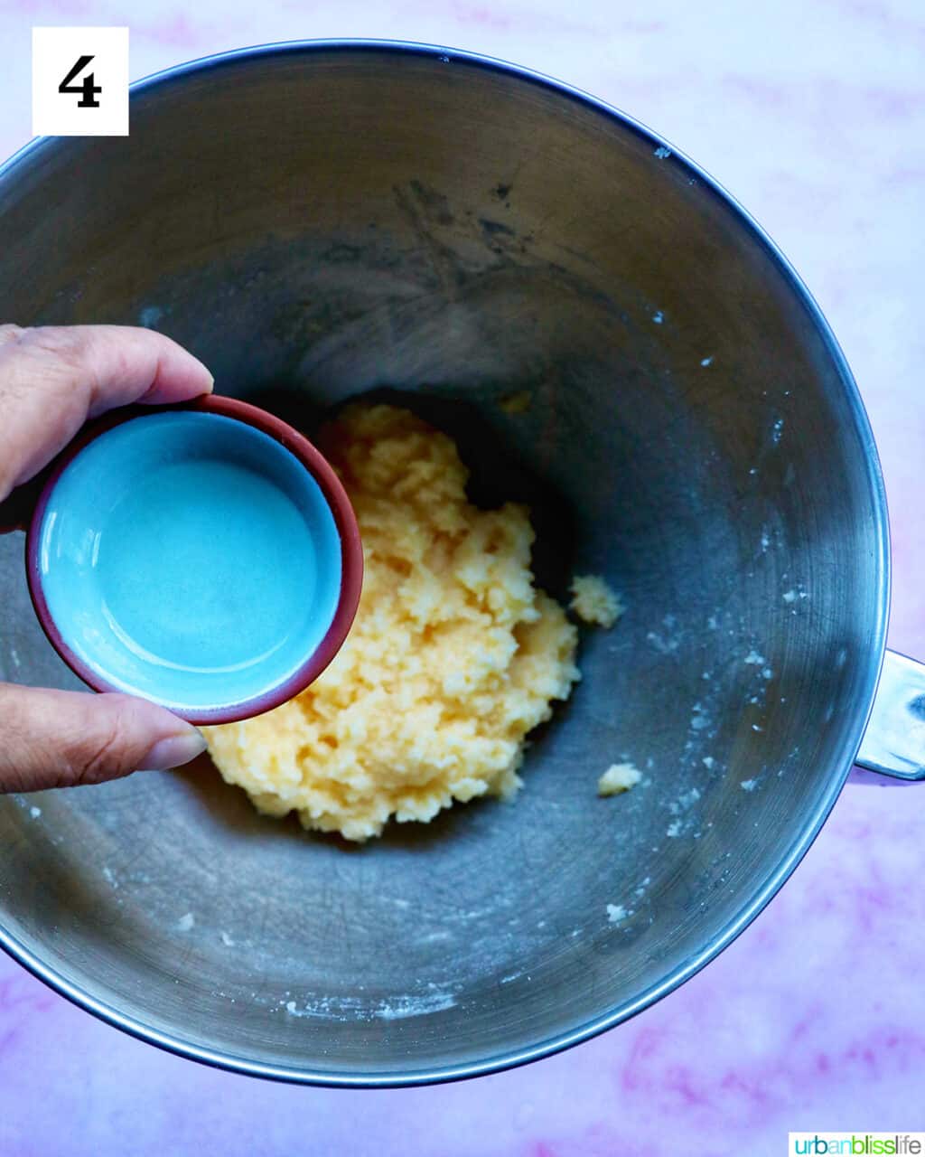 hand holding a bowl of liquid over cookie batter in a bowl.