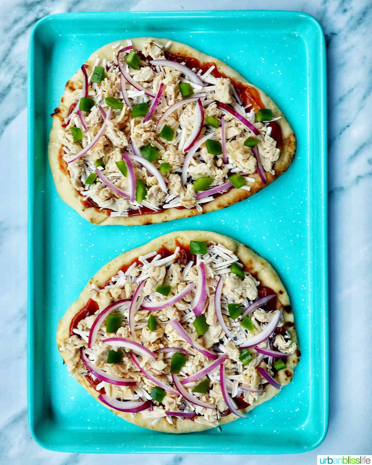 two barbecue chicken flatbread pizzas on a blue baking sheet.