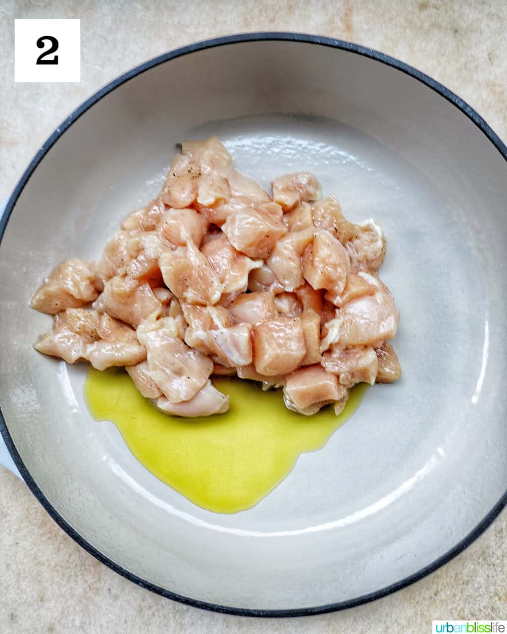 chunks of raw chicken cooking in olive oil in a large skillet.