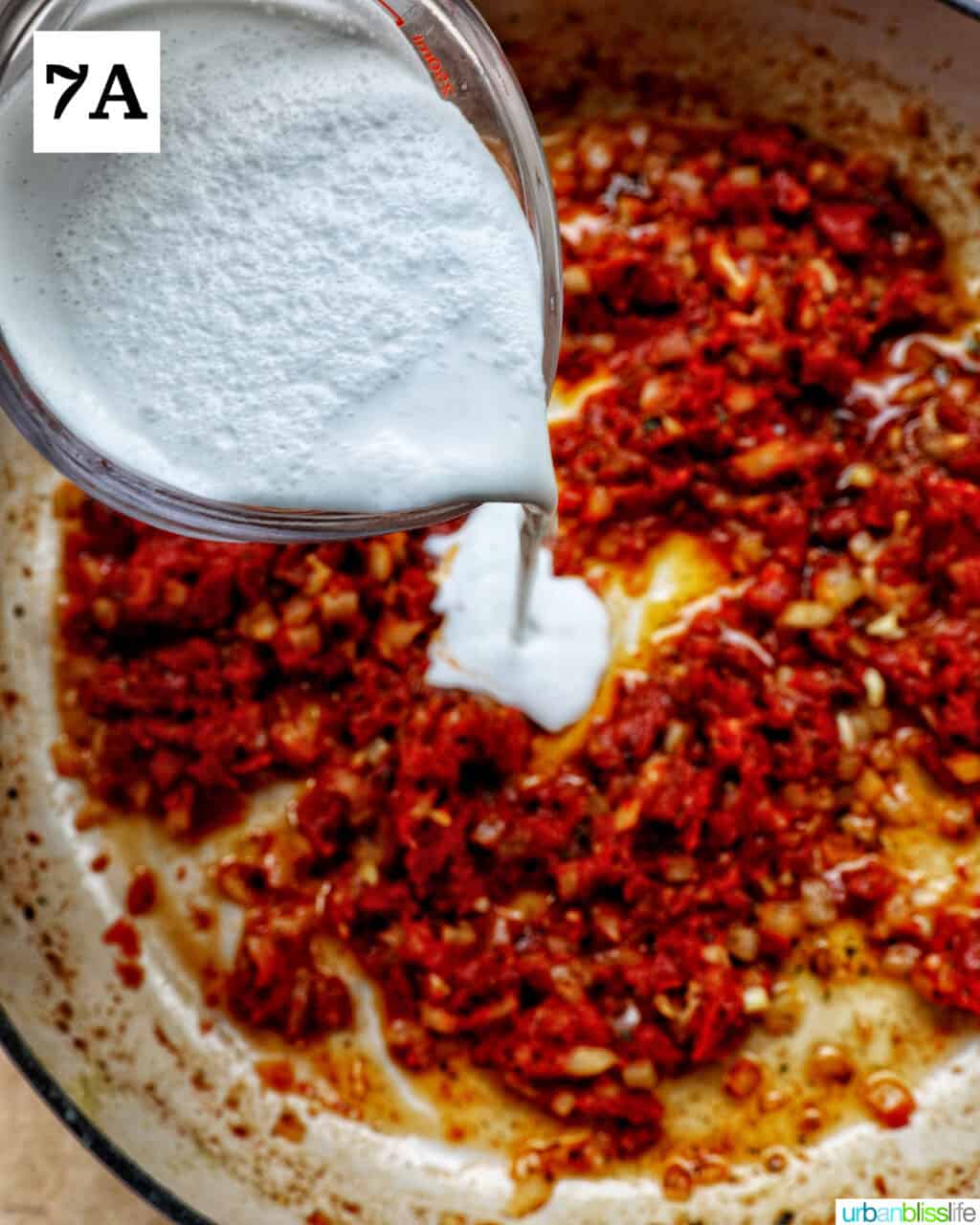 cup of heavy cream pouring into a skillet of diced onions and chopped sun-dried tomatoes.
