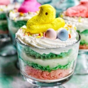 easter trifle with layers of colored cake, shredded coconut, vanilla pudding, and easter candies in a parfait glass