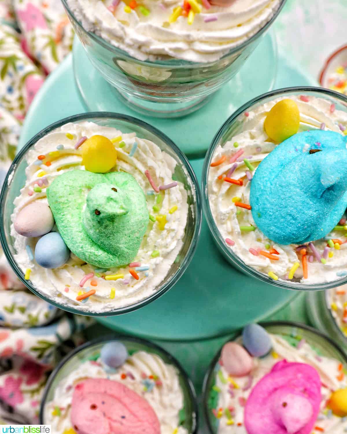 Set of Easter trifles with layers of pastel colored cake, shredded coconut, vanilla pudding, and whipped cream, topped with colorful Easter candies.