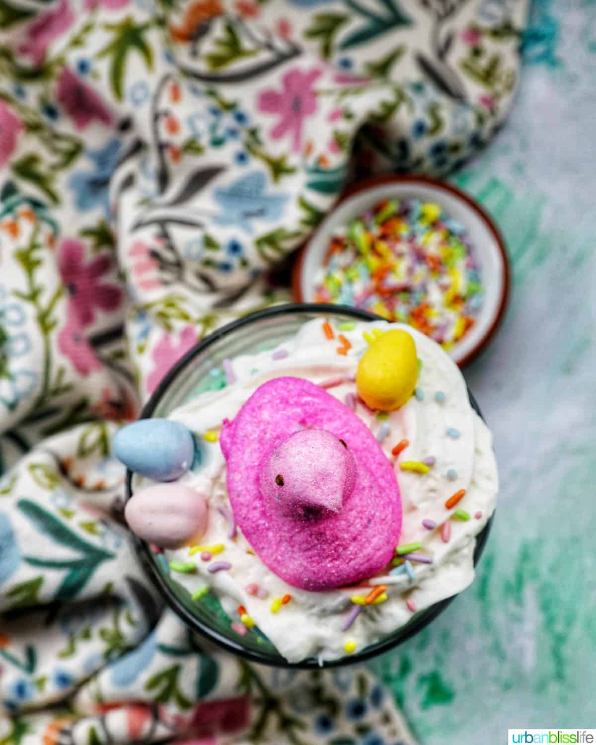 Easter trifle with layers of pastel colored cake, shredded coconut, vanilla pudding, and whipped cream, topped with colorful Easter candies.