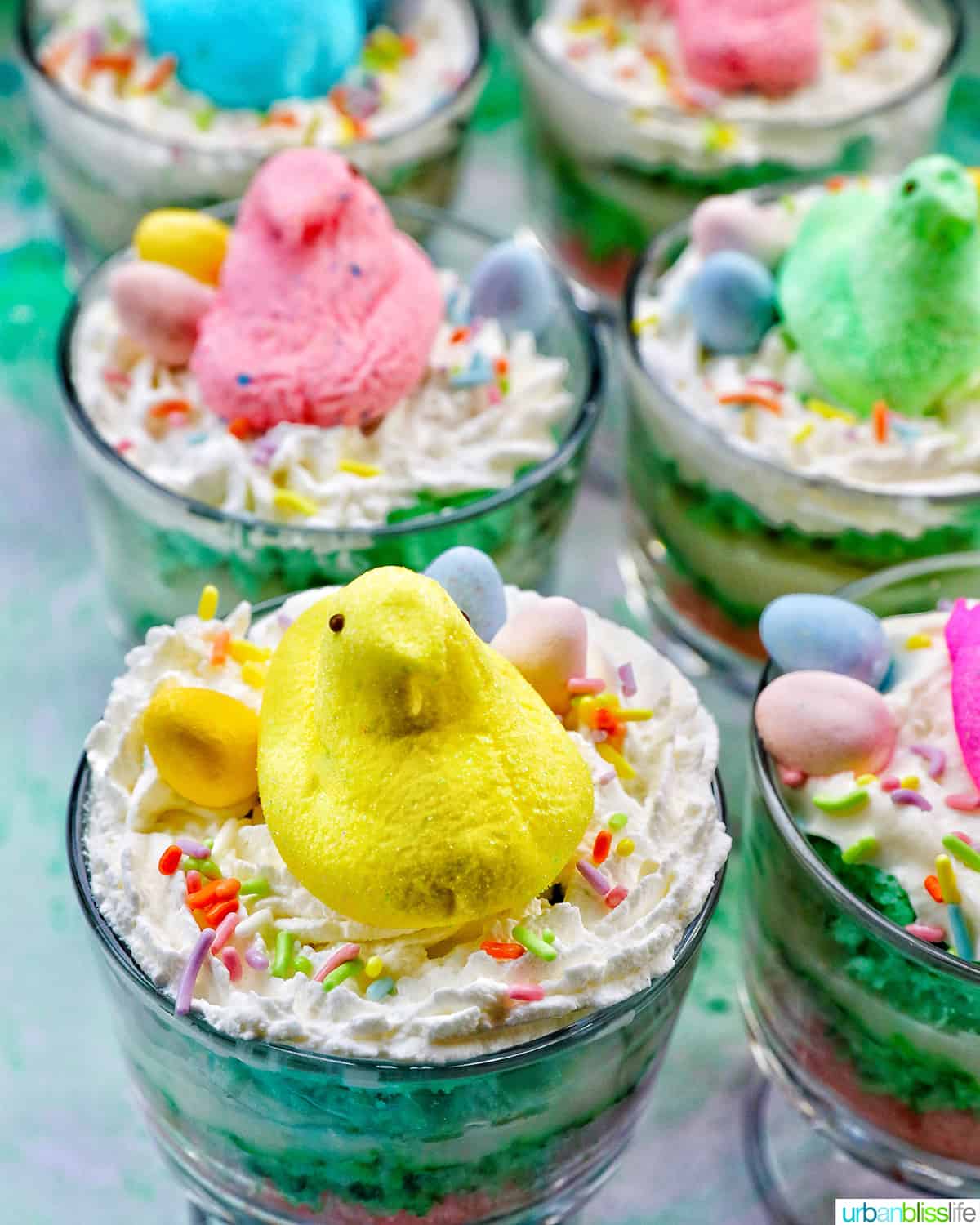 Set of Easter trifles with layers of pastel colored cake, shredded coconut, vanilla pudding, and whipped cream, topped with colorful Easter candies.