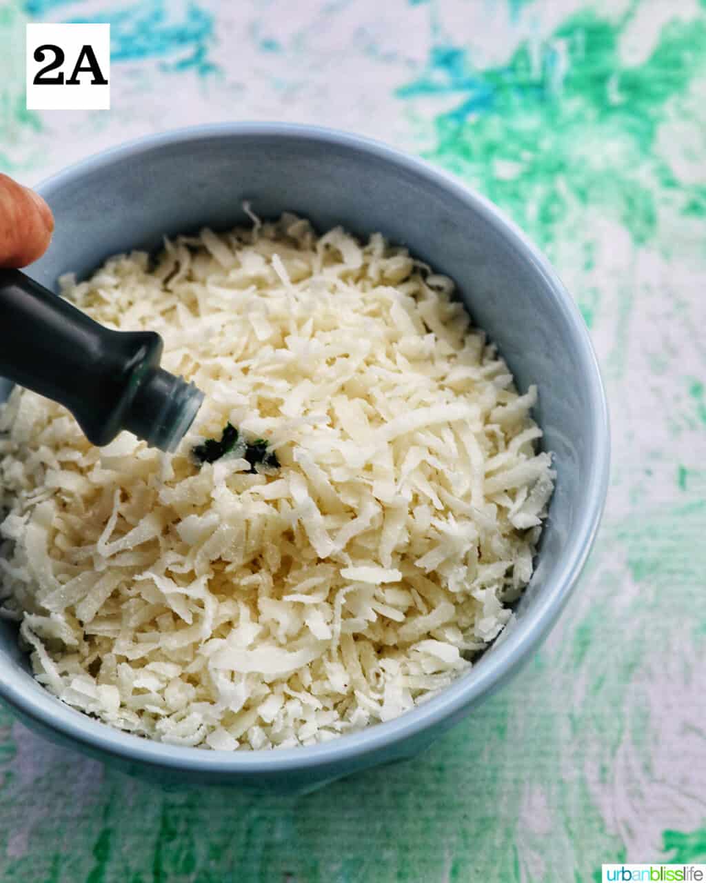 adding green food coloring to white shredded coconut in a bowl.