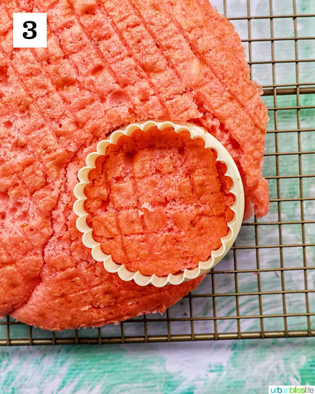 round cookie cutter placed over a pink cake on wire rack.