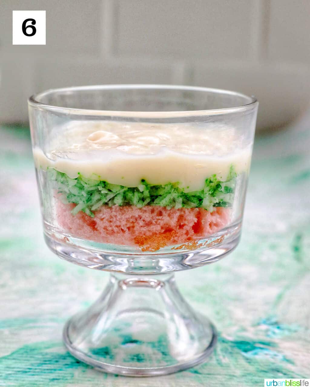 vanilla pudding over shredded coconut over a layer of pink cake in a trifle bowl.